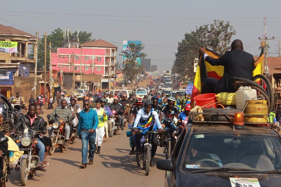 Urban welcome parade with cyclists, motorcade, and crowds lining the street
